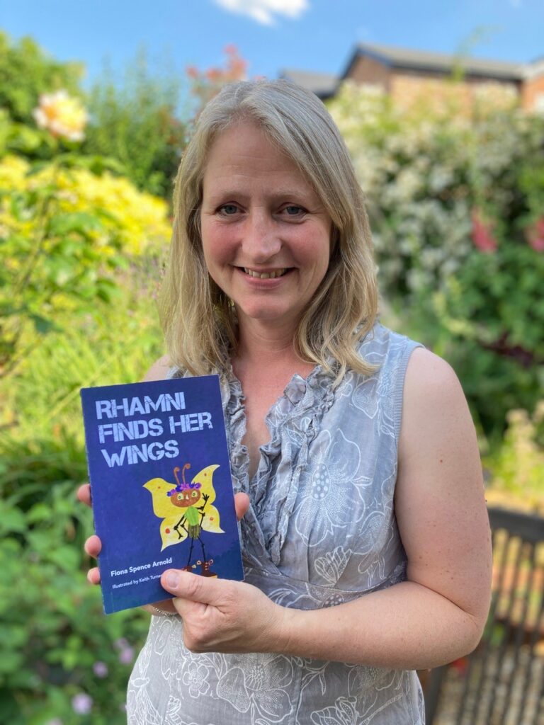 A photograph of Fiona Spence-Arnold, a previous Writing East Midlands mentee and children's author, with her recent debut novel, Rhamni Finds Her Wings.